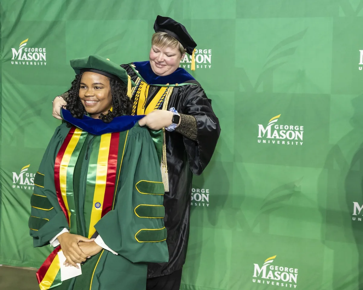 A faculty advisor hoods a doctoral candidate during the 2023 Winter Commencement at EagleBank Arena.